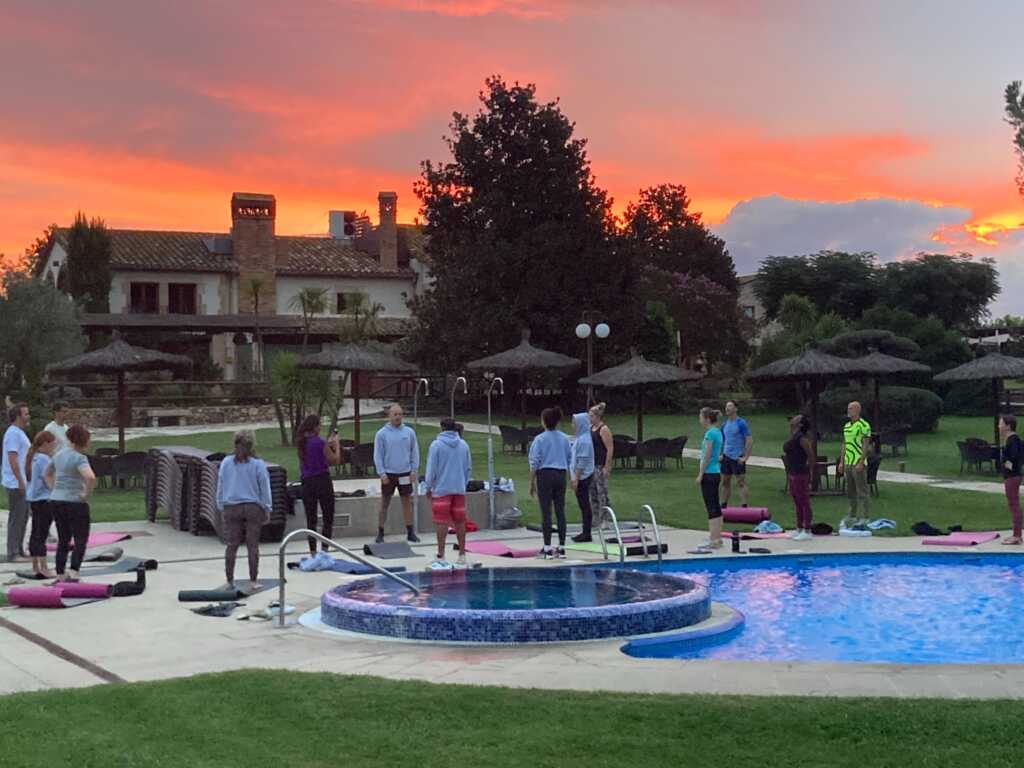 AQai retreat participants engaged in a wellness or team-building session by the pool at sunrise, with conference planning tools supporting the organization of the event.