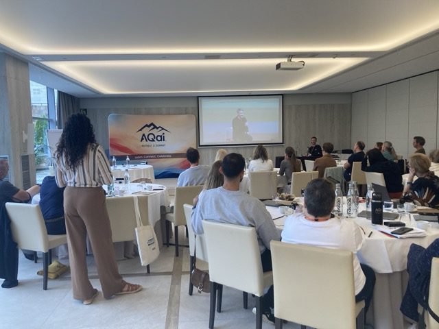 AQai event participants listening attentively to a speaker during a presentation in a conference room.